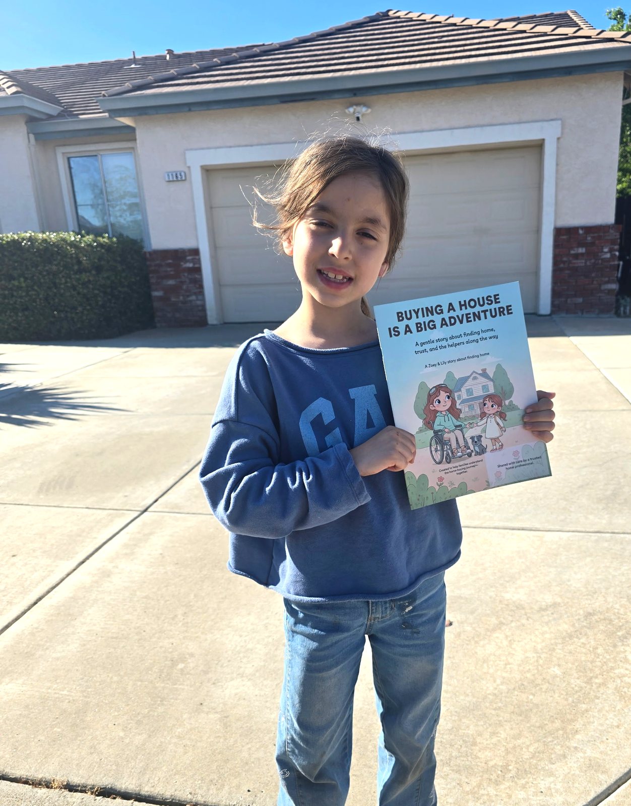 Young reader holding the book outside her new home